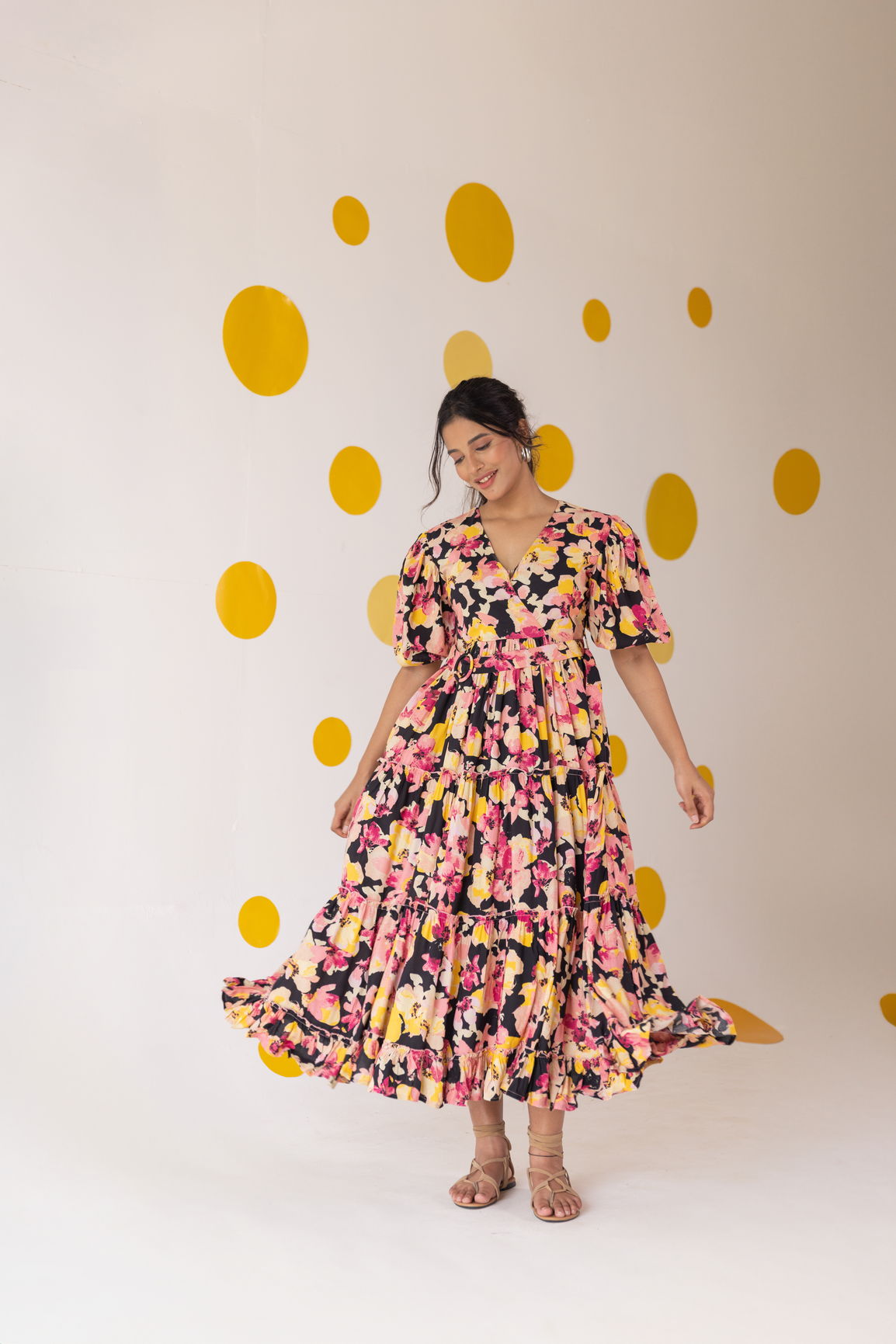 Model twirling in a floral tiered cotton maxi dress against a yellow polka dot background.