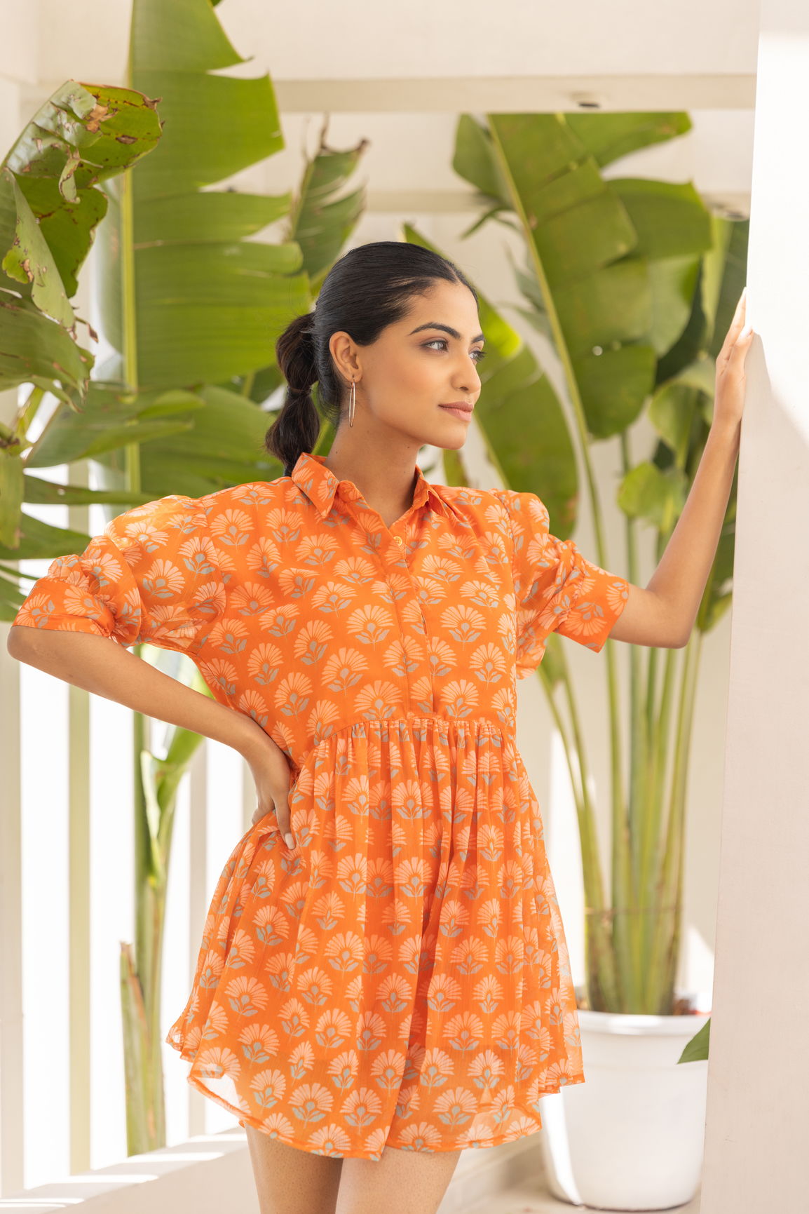 Model wearing an orange candy mini dress in a tropical setting.