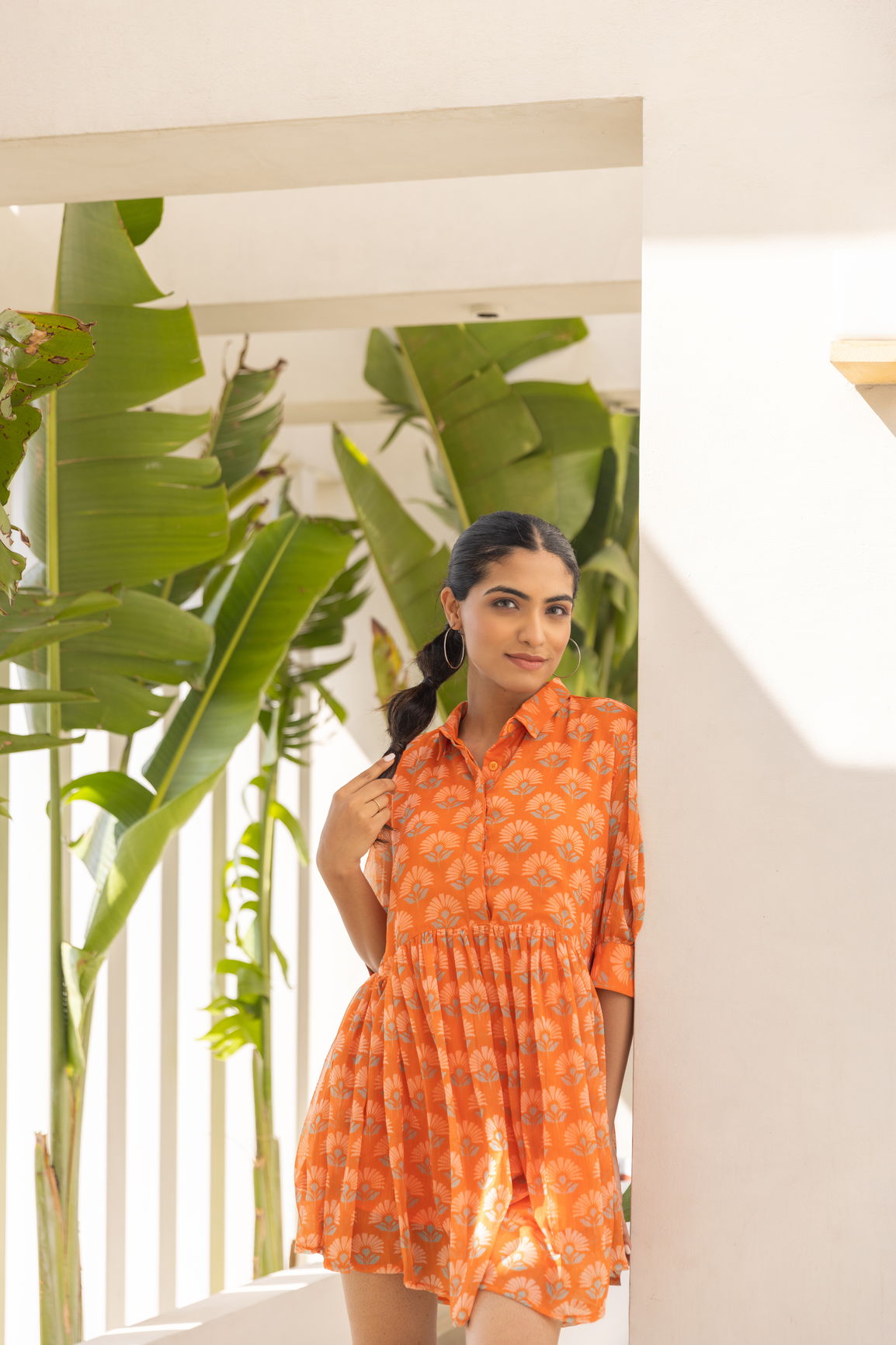 Model wearing an orange candy mini dress among tropical plants.