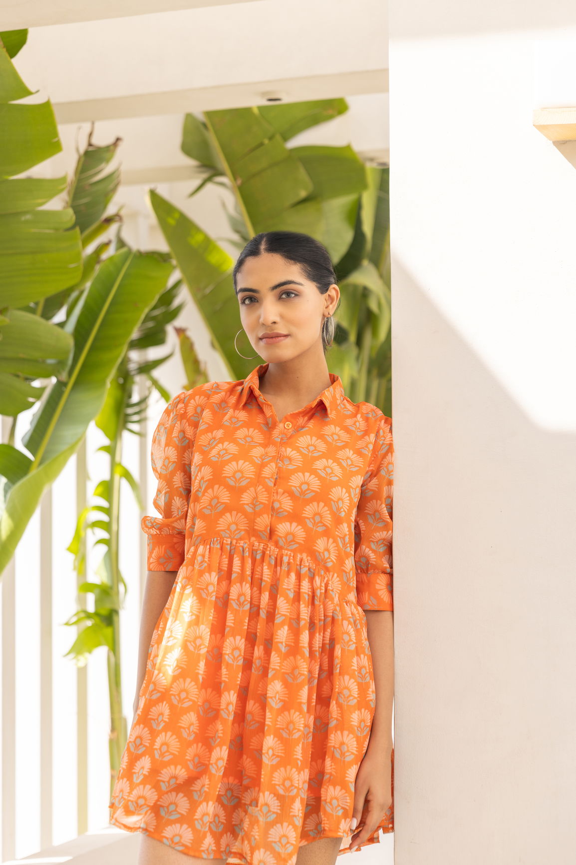 Model in orange floral mini dress against tropical background.