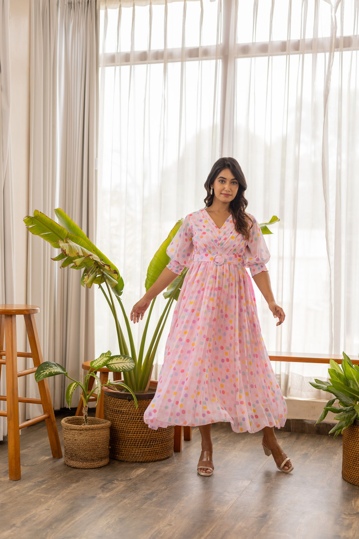 Model wearing a pink polka pleated maxi dress in a bright room.