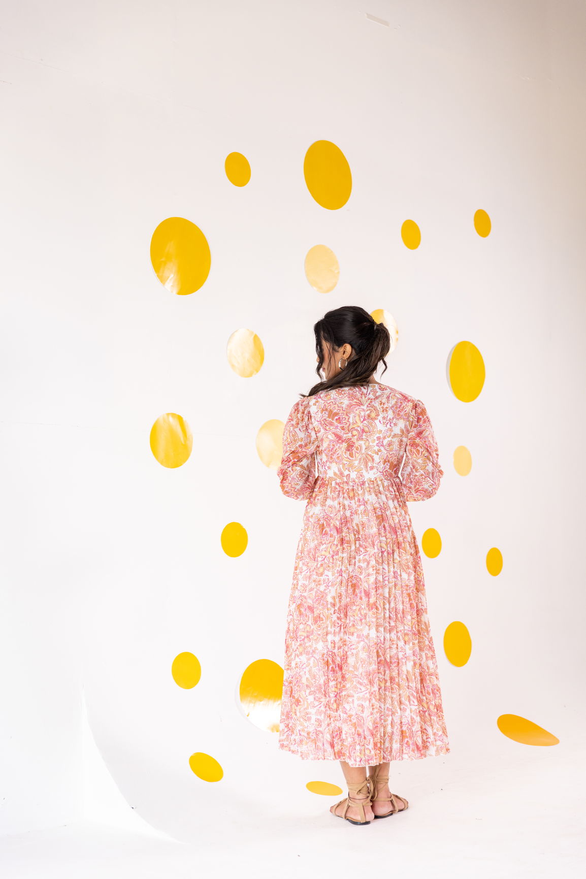 Woman in pleated motif maxi dress against yellow dot backdrop.