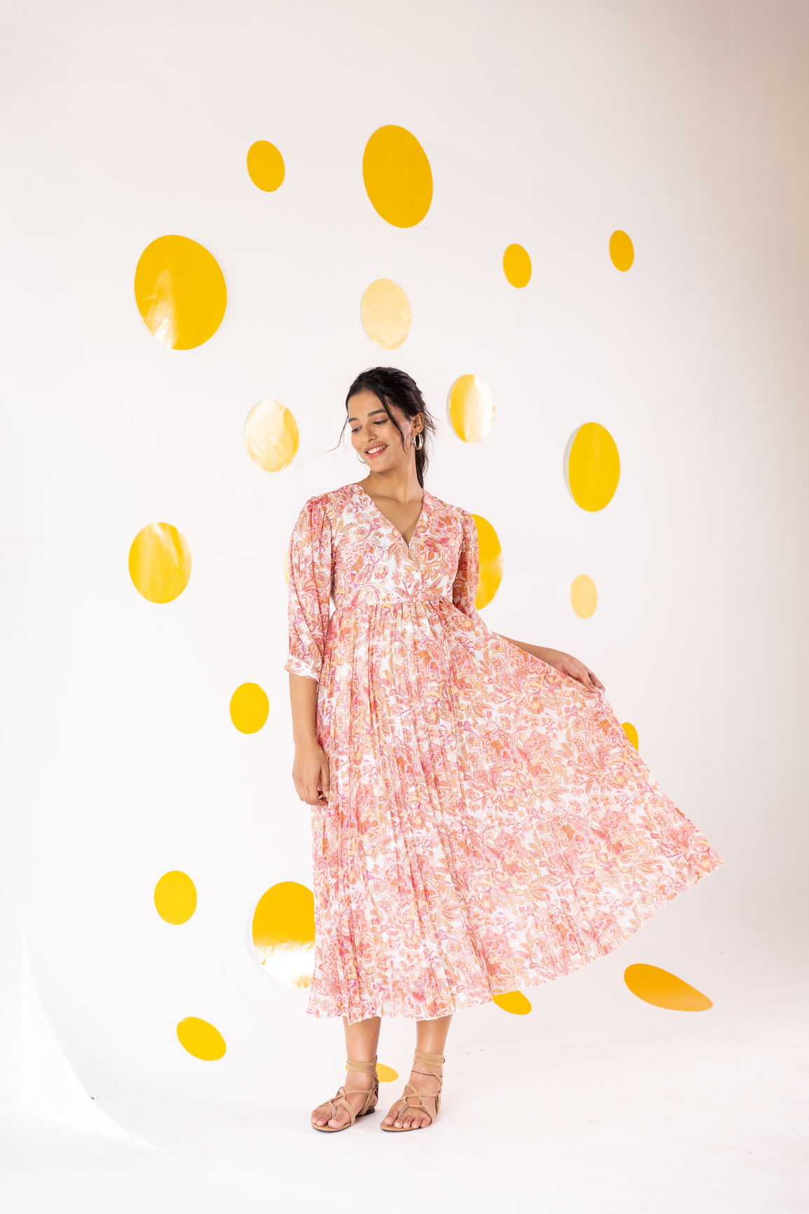 Woman wearing pleated motif maxi dress against yellow polka dot background.