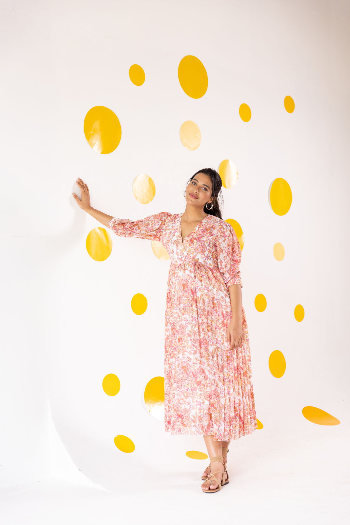 Model wearing Pleated Motif Maxi dress against vibrant yellow polka dot wall.