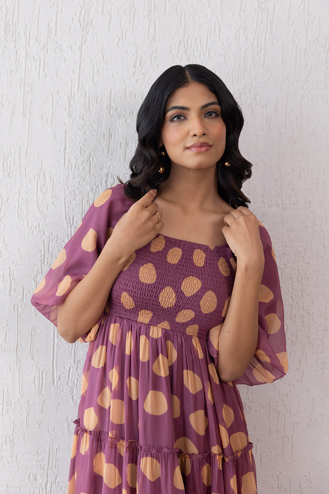 Woman wearing salmon polka dot maxi dress against textured wall.