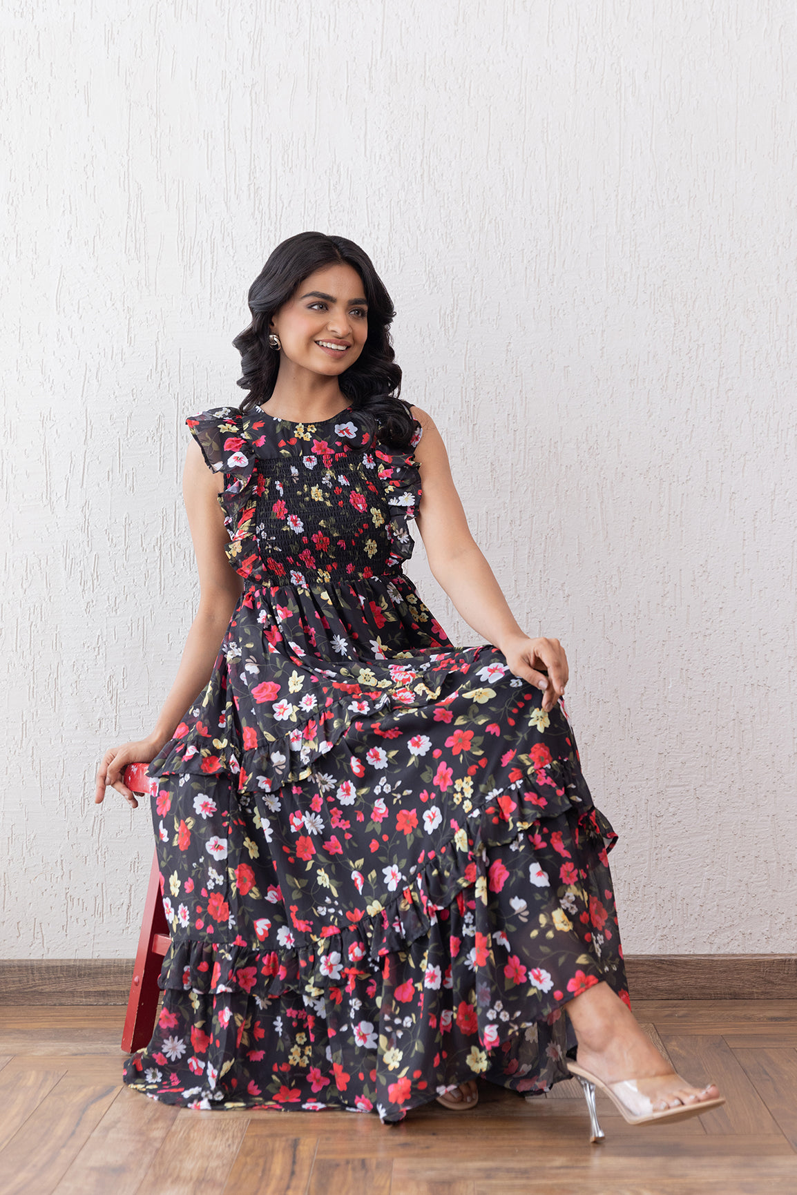 Elegant woman in black floral smocked maxi dress, sitting gracefully.