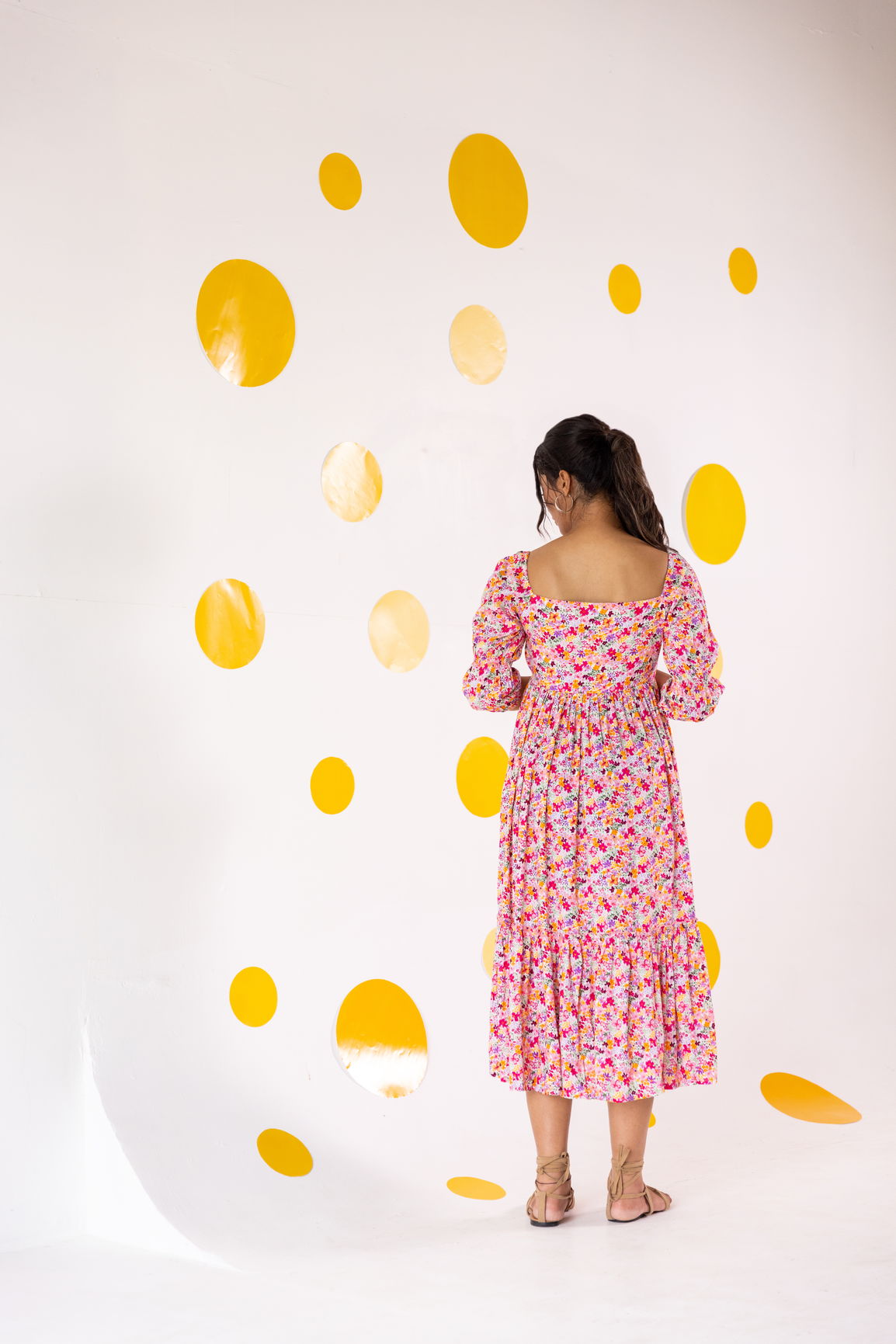Woman in floral cotton maxi dress against yellow polka dot wall.
