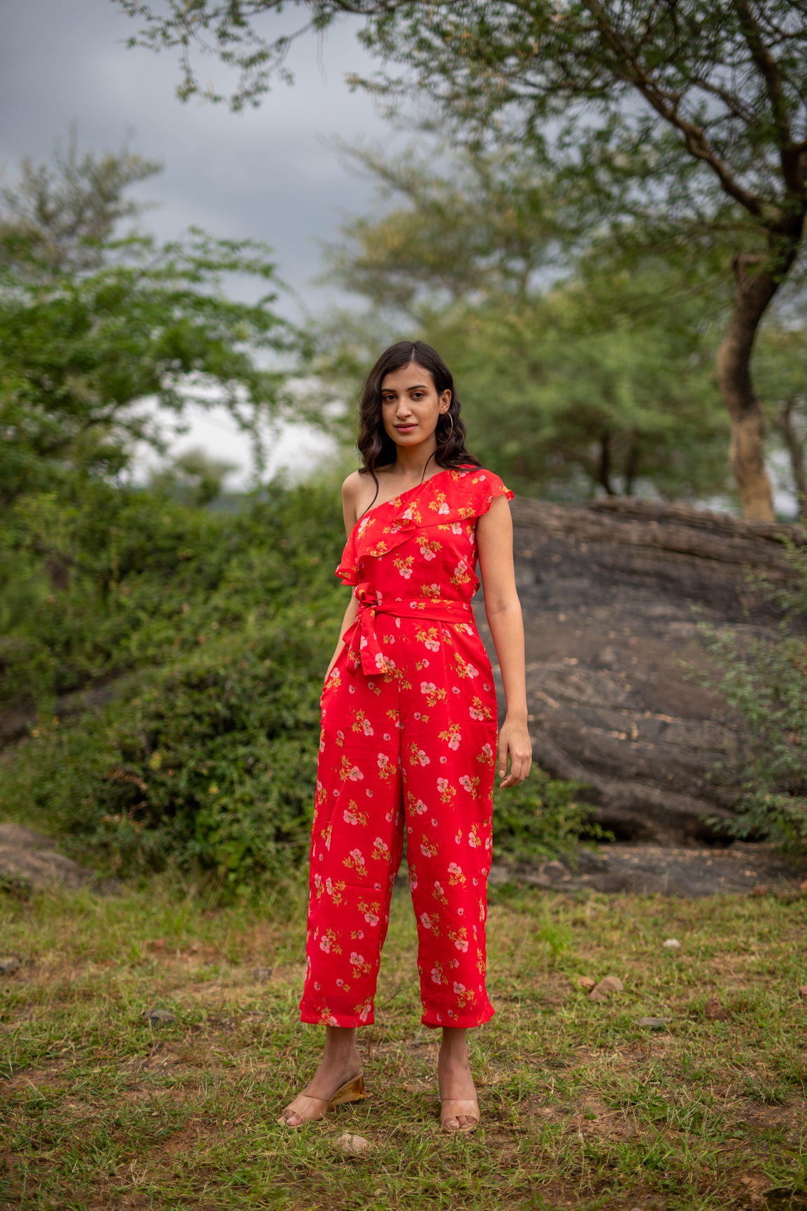 Floral one-shoulder jumpsuit in vibrant red outdoors.