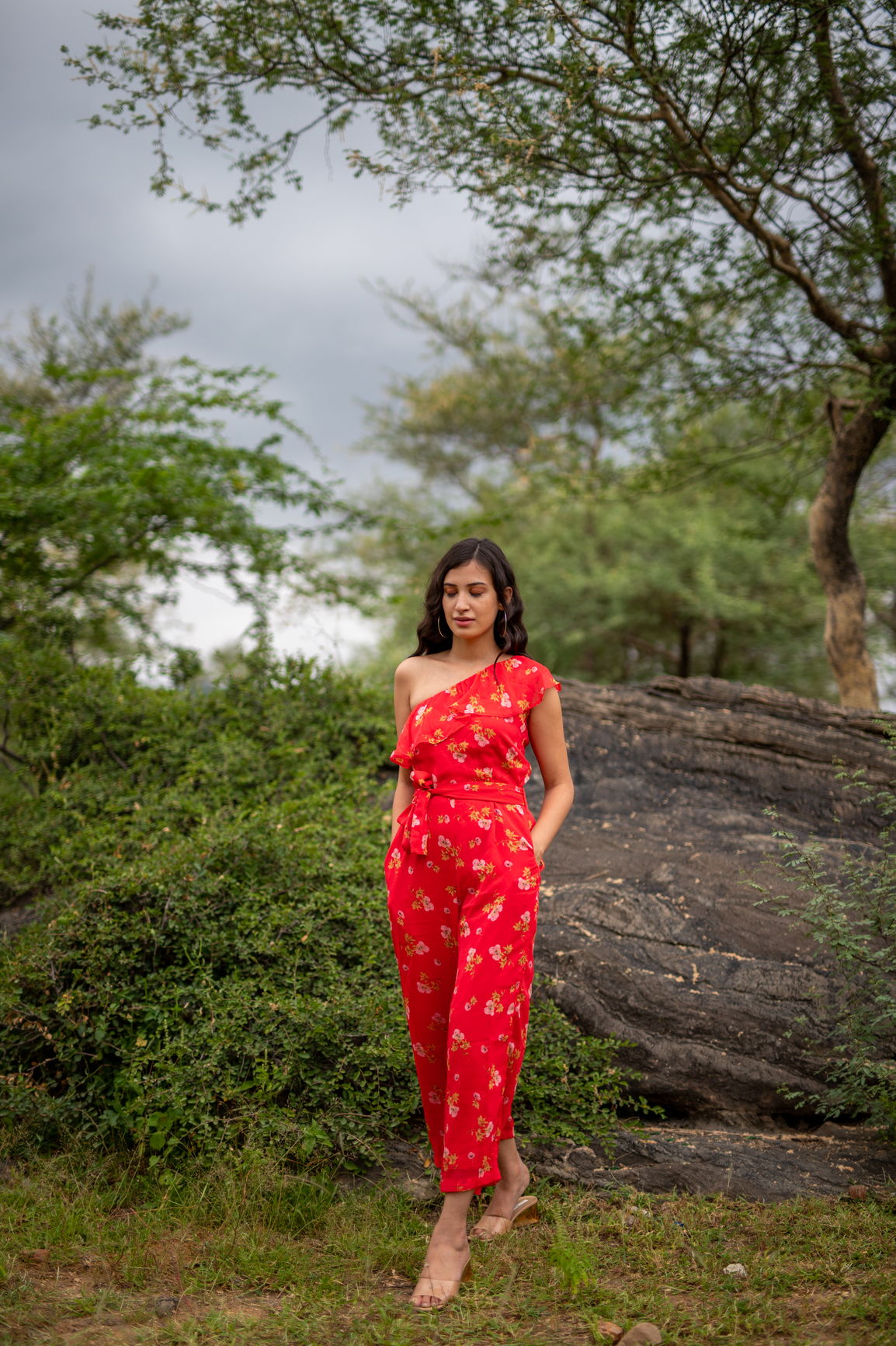 Floral one-shoulder jumpsuit worn outdoors with stylish casual footwear.