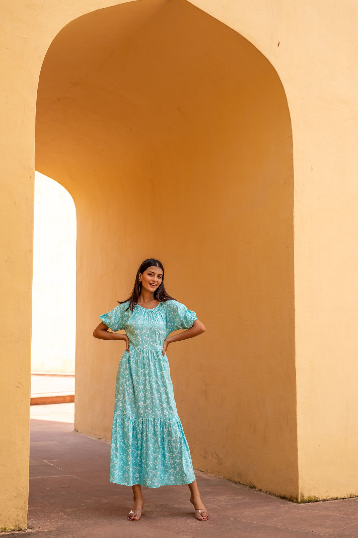 Woman wearing a sea blue floral maxi dress in a sunny archway.