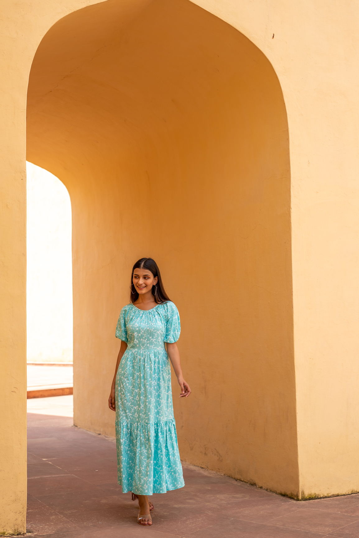 Woman wearing sea blue floral maxi dress in architectural setting.