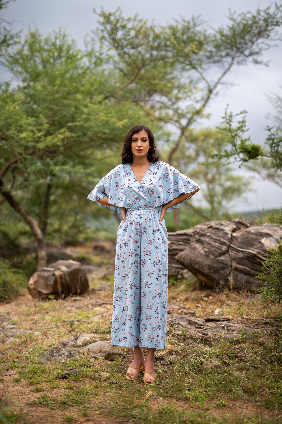 Sky blue floral jumpsuit worn by model in nature setting.