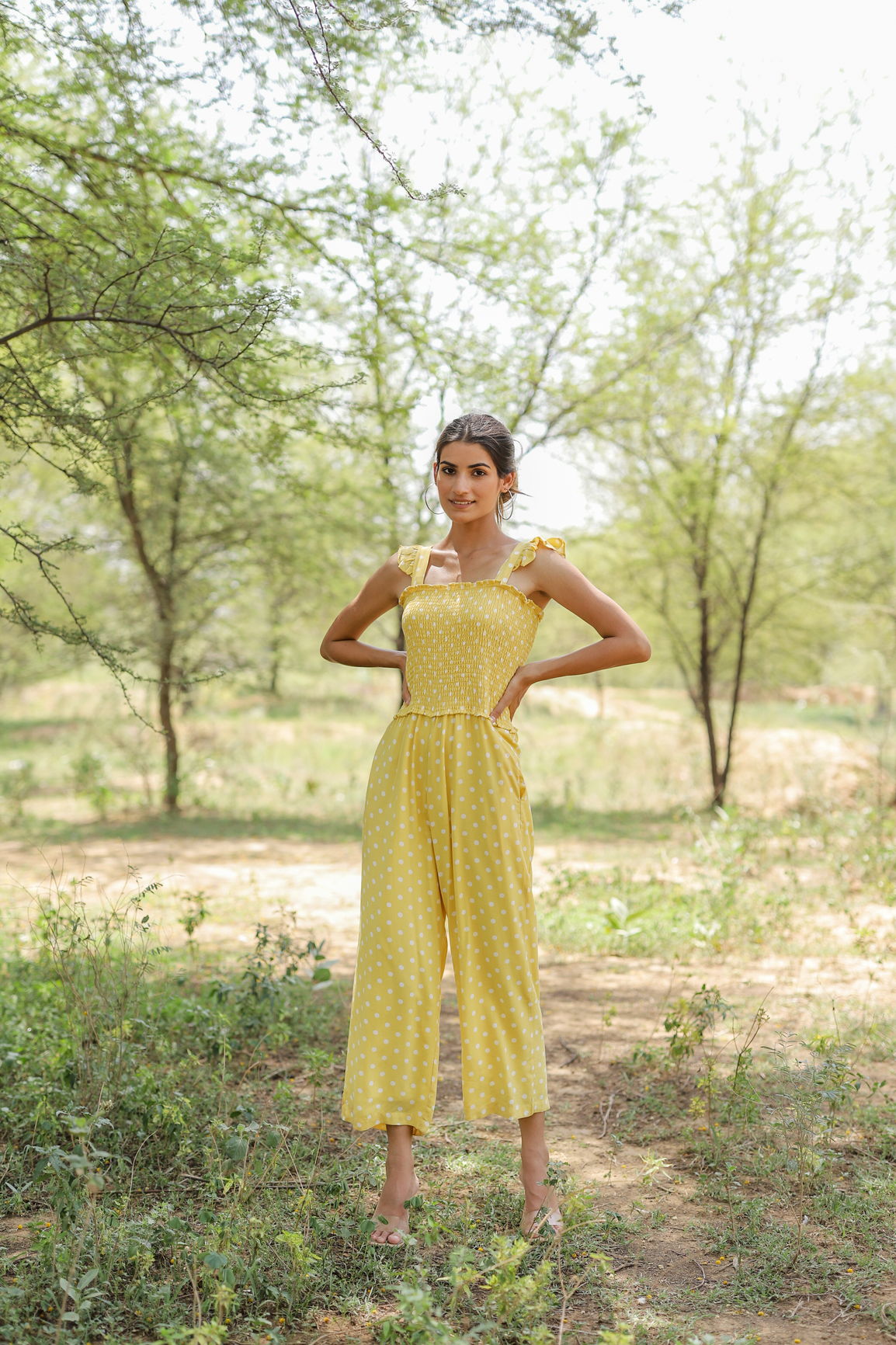 Yellow polka dot jumpsuit worn outdoors with natural greenery background.