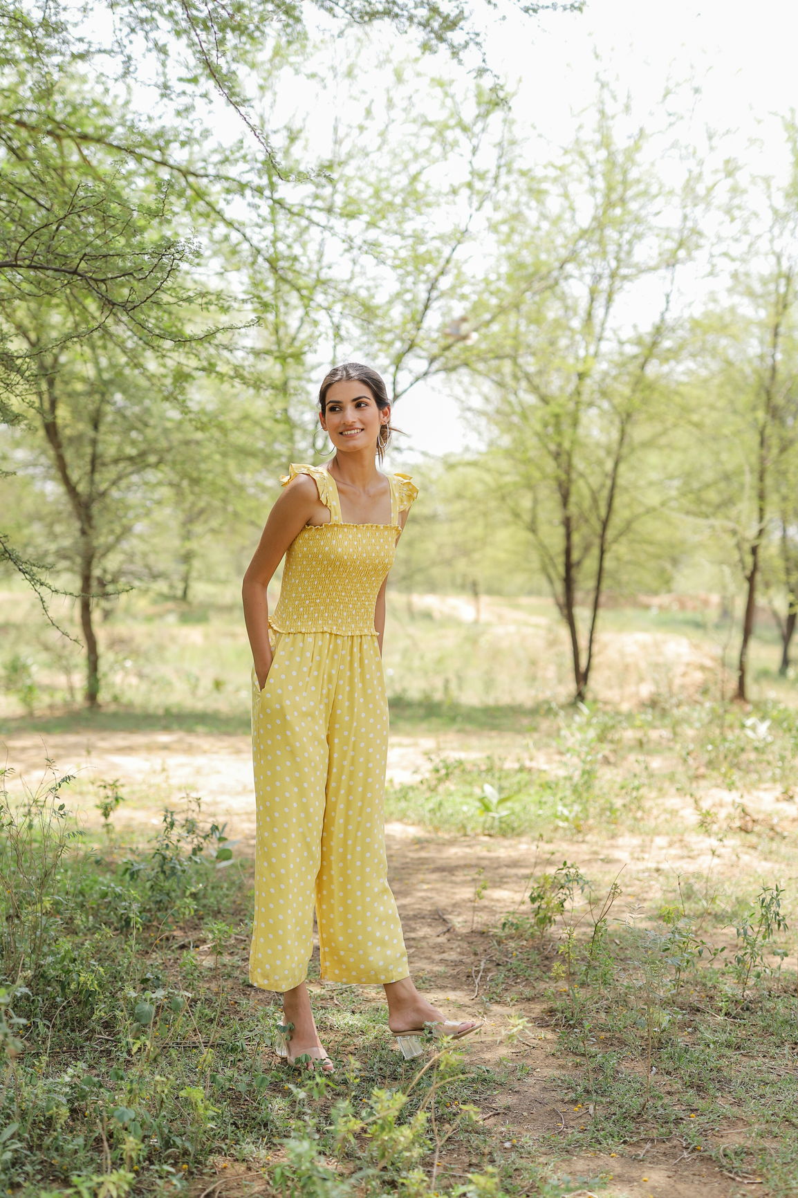 Young woman wearing a yellow polka dot jumpsuit in nature.