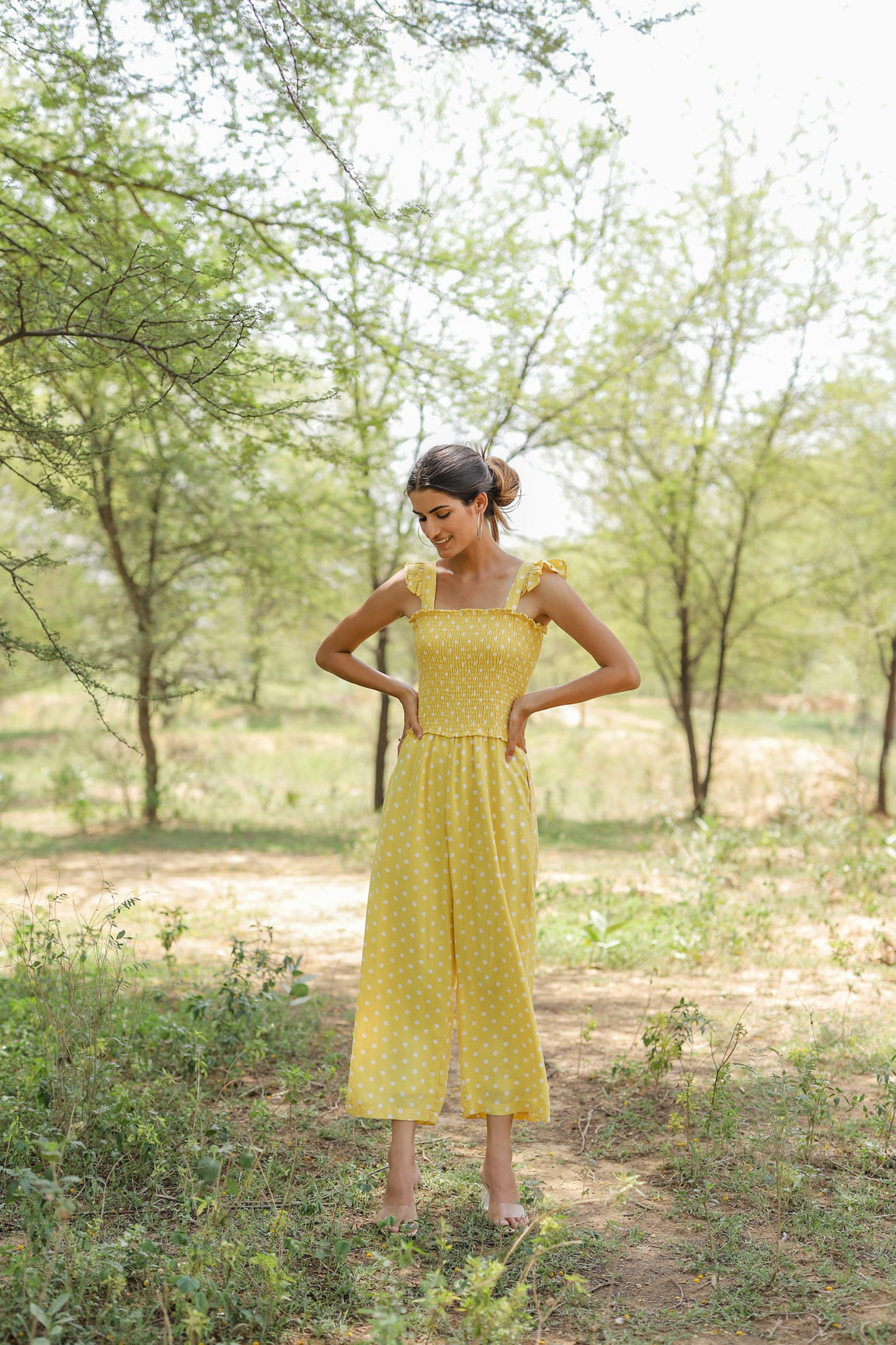 Yellow polka dot jumpsuit worn outdoors with greenery backdrop.