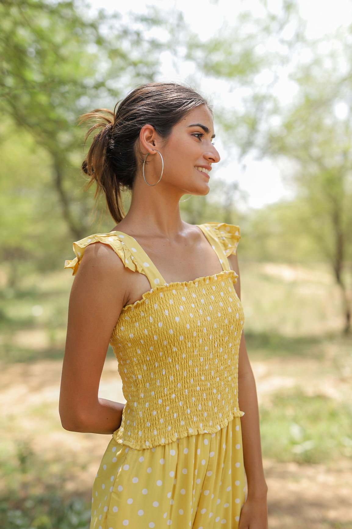 Yellow polka dot jumpsuit model smiling outdoors in natural light.