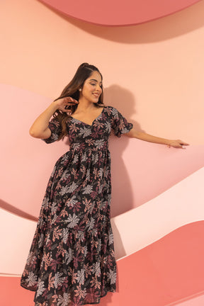 Woman wearing a black floral maxi dress against a pink background.