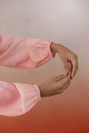 Elegant hands adjusting the MARBLE MAXI's flowing pink sleeves.