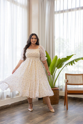 Elegant woman in floral MINIMAL MAXI - POLAGO PLUS dress, bright indoor setting.