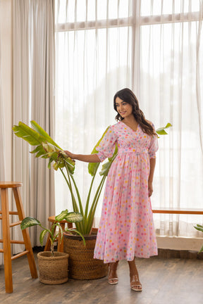 Model in pink polka pleated maxi dress near green plants.