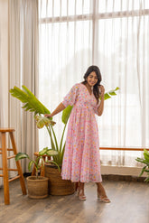 Woman in pink polka pleated maxi dress standing by plants.