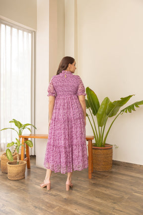 Back view of a woman wearing a pink smocked nursing maxi dress.