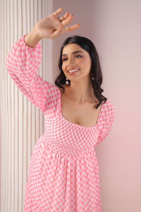 Smiling woman in pink gingham maxi dress posing playfully.