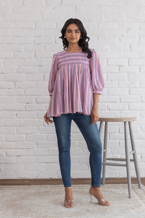 Pink striped cotton top worn with jeans against a white brick wall.