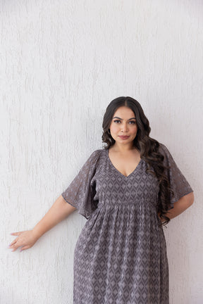 Woman in grey jacquard maxi dress against textured white wall.