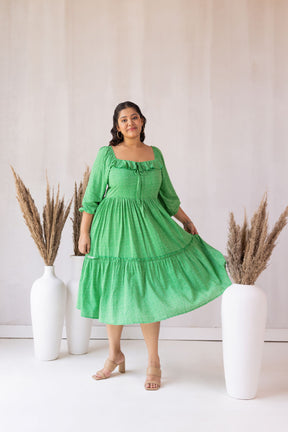 Woman in green dress poses beside elegant vases and plants.