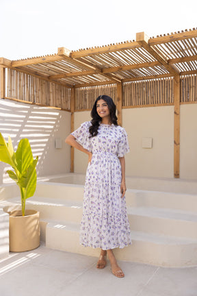Elegant woman in white chiffon floral maxi dress with vibrant greenery.