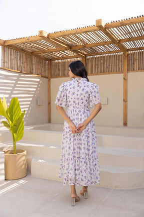 Elegant woman wearing white chiffon maxi dress with floral design.