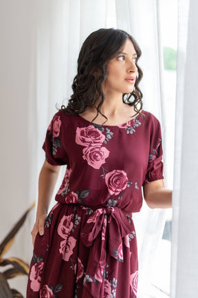 Wine floral co-ord dress with elegant roses, model by window.