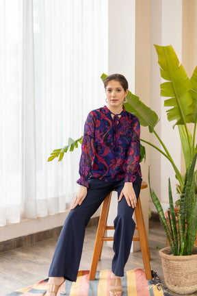 Elegant woman in floral MIDNIGHT DAWN TOP, styled with navy trousers.