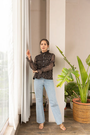 Elegant woman in ruffle top paired with light jeans indoors.