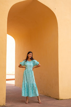 Woman wearing a sea blue floral maxi dress in a sunny archway.