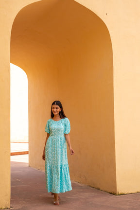 Woman wearing sea blue floral maxi dress in architectural setting.