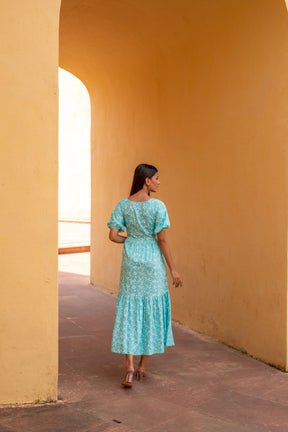 Woman in a sea blue floral maxi dress against a yellow wall.