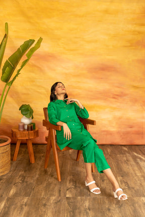 Model wearing vibrant green shamrock co-ord set, sitting in stylish chair.
